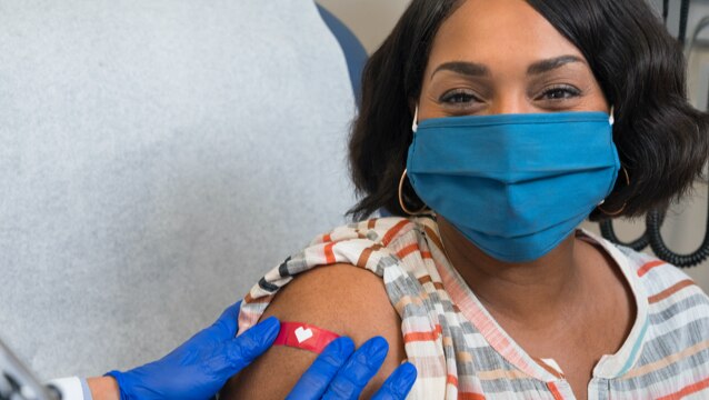 image of woman in a face covering smiling while healthcare worker applies a bandage after COVID-19 vaccination